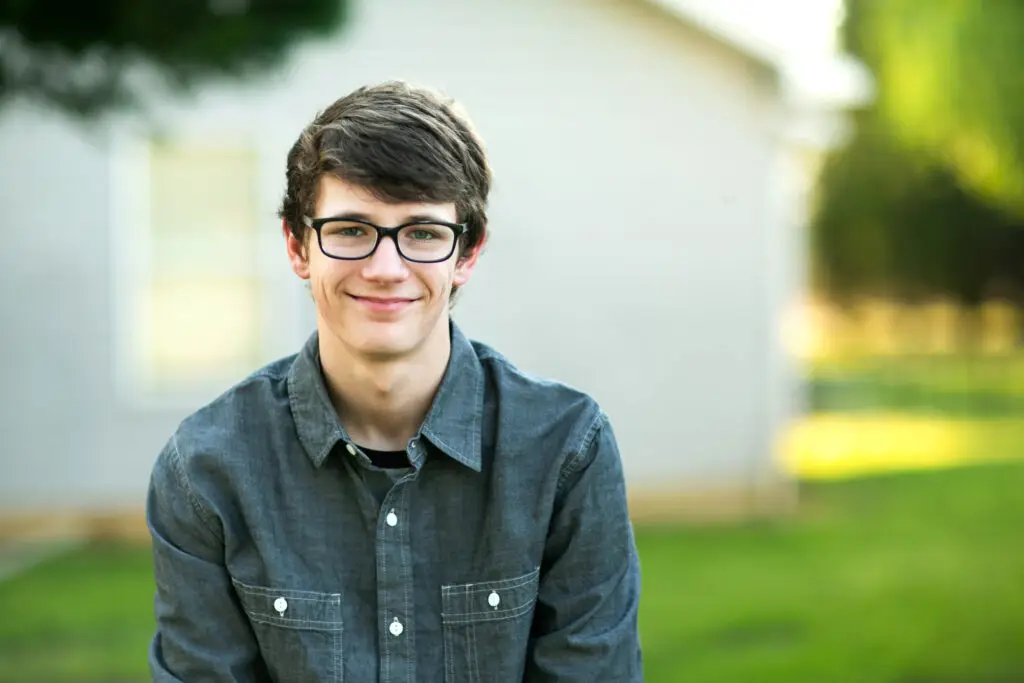 Teenage Boy with Glasses Outside on a spring day sitting outside of a house home smiling