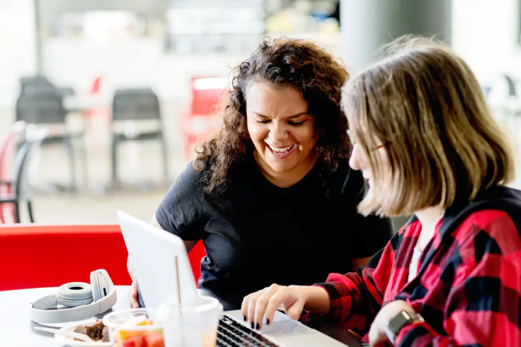 Two women sit in a cafe and edit an essay together
